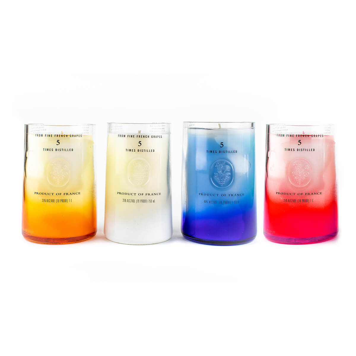 Four Recycled Vodka Candle – Multi-color glass candles in ombre orange, white, blue, and pink are lined up side by side, each with “Product of France” and measurement details on the front. These natural soy candles add vibrant charm to any space.