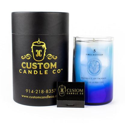 A Recycled Vodka Candle – Multi-color in a glass jar is displayed beside a black cylindrical "Custom Candle Co" box and a small black matchbox.