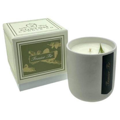 The Holiday Scented Boxed Candle – Frasier Fir Scent is a white soy wax candle in a ceramic container with gold and green accents, paired with a matching box—ideal for adding festive fragrance to your home.