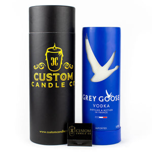 A Recycled French Vodka Candle - Blue from Custom Candle Co. in a black cylindrical box stands beside a blue vodka bottle, while a small branded matchbox highlights its eco-friendly, natural soy candle origins.