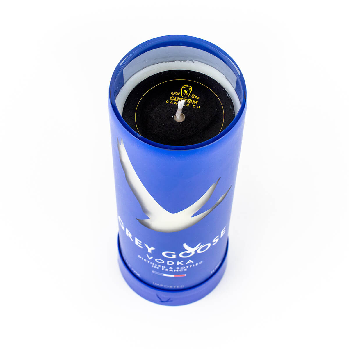 The Recycled French Vodka Candle - Blue is a blue cylindrical container upcycled from a French vodka bottle, filled with natural soy wax and featuring a caution sticker near the wick.
