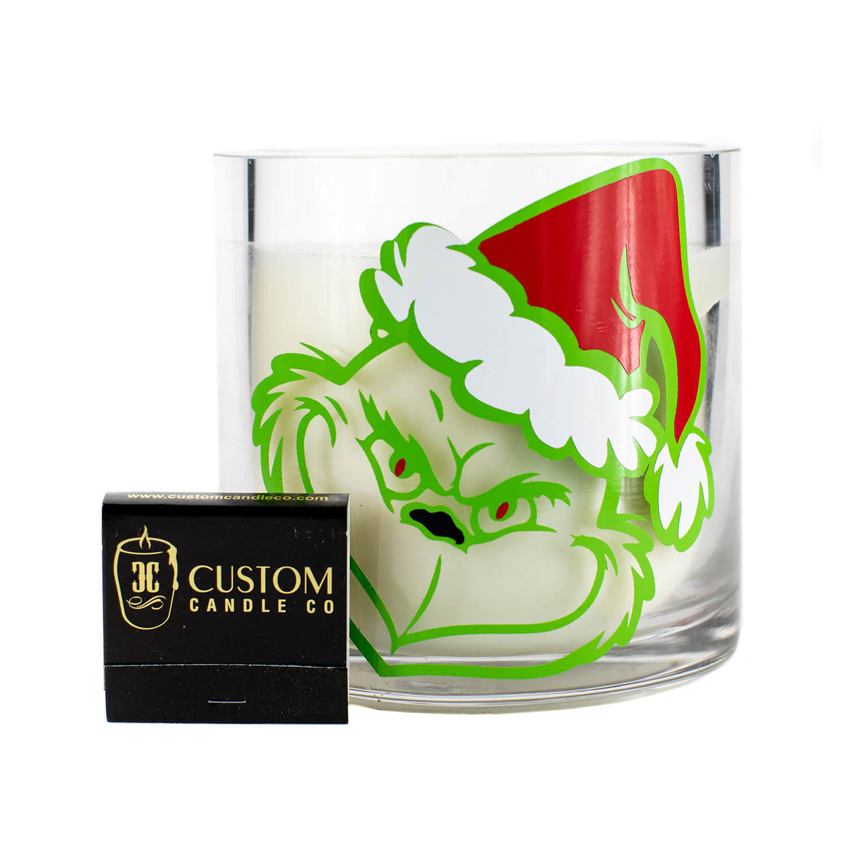 The Grinch Holiday Candle includes a glass holder with the Grinch in a Santa hat and a black "Custom Candle Co." matchbox, making it the perfect festive accent for any holiday space.