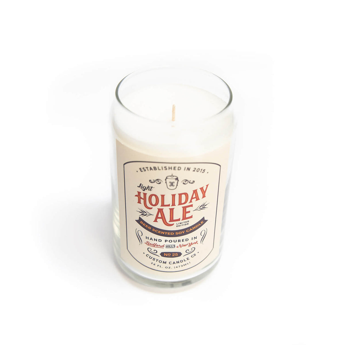 The Light Holiday Ale Candle is a hand-poured natural soy candle in a clear glass with “Holiday Ale” label and decorative text, displayed on a white background.