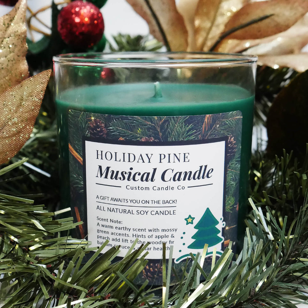 A green-scented soy "Musical Holiday Candle – Holiday Pine" is displayed with artificial pine, gold leaves, and red and green ornaments—an ideal pick for anyone who loves musical Christmas candles.