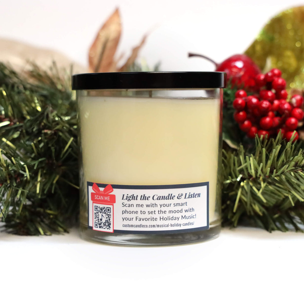 The Musical Holiday Candle & Diffuser | Holiday Sparkle is a white scented soy candle in a glass jar with a black lid, festive pine branches, red berries, and a gold ornament. The label features text and a QR code for the holiday season.