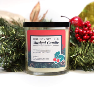 The Musical Holiday Candle & Diffuser | Holiday Sparkle features festive decorations, a black lid, and sits among greenery and berries—a delightful scented soy candle perfect for holiday celebrations.