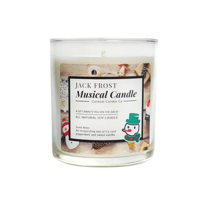The Musical Holiday Candle – Jack Frost is a clear glass, all-natural soy candle featuring a snowman illustration, peppermint and vanilla scent, and plays music for a festive holiday touch.