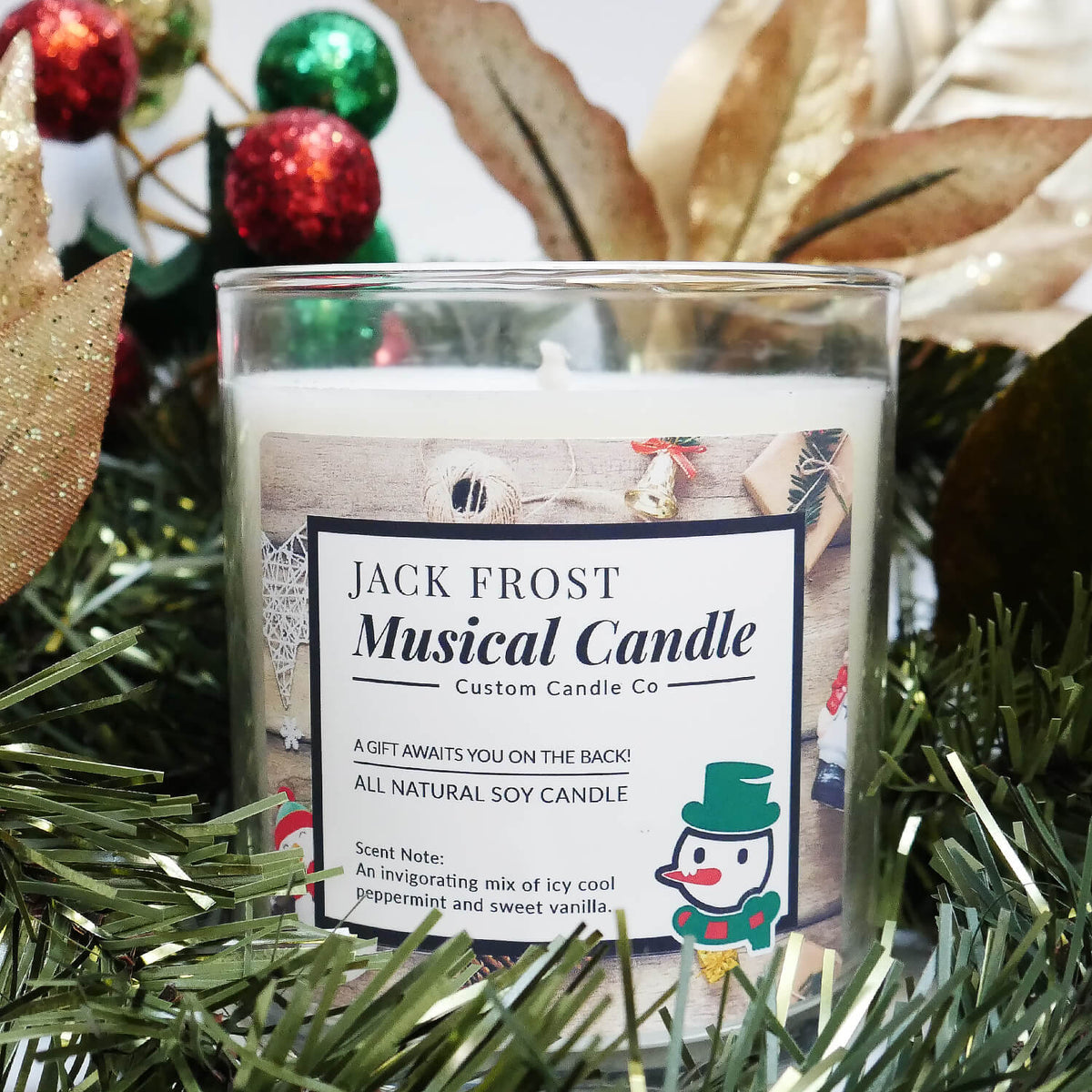 The Musical Holiday Candle – Jack Frost sits among green artificial pine, gold leaves, and red and green ornaments—perfect for capturing the festive spirit of soy and scented holiday candles in a decorative glass jar.