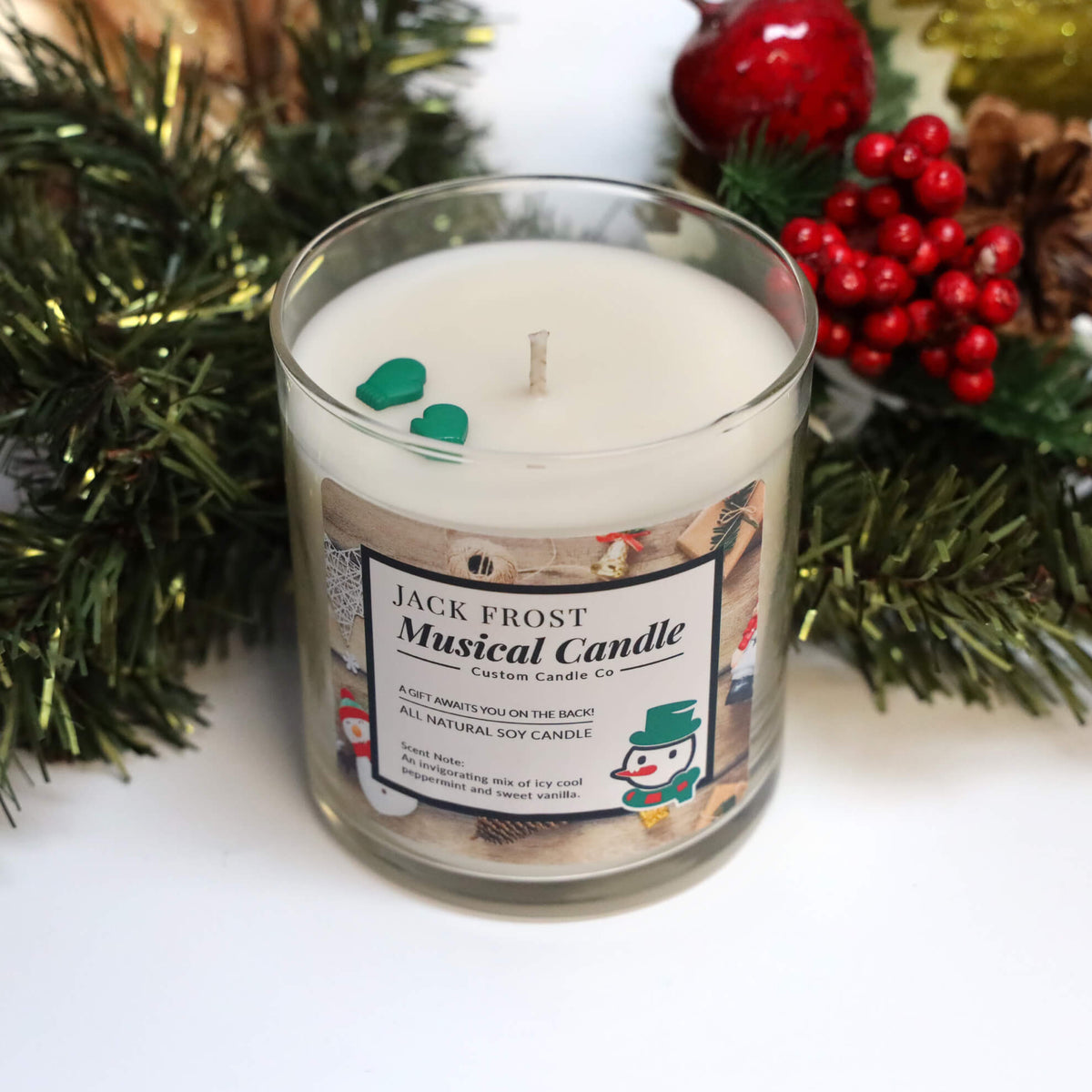 The Musical Holiday Candle & Diffuser | Jack Frost features festive greenery, red berries, and green mitten decorations in the wax—perfect for adding charm to your scented candle collection this holiday season.
