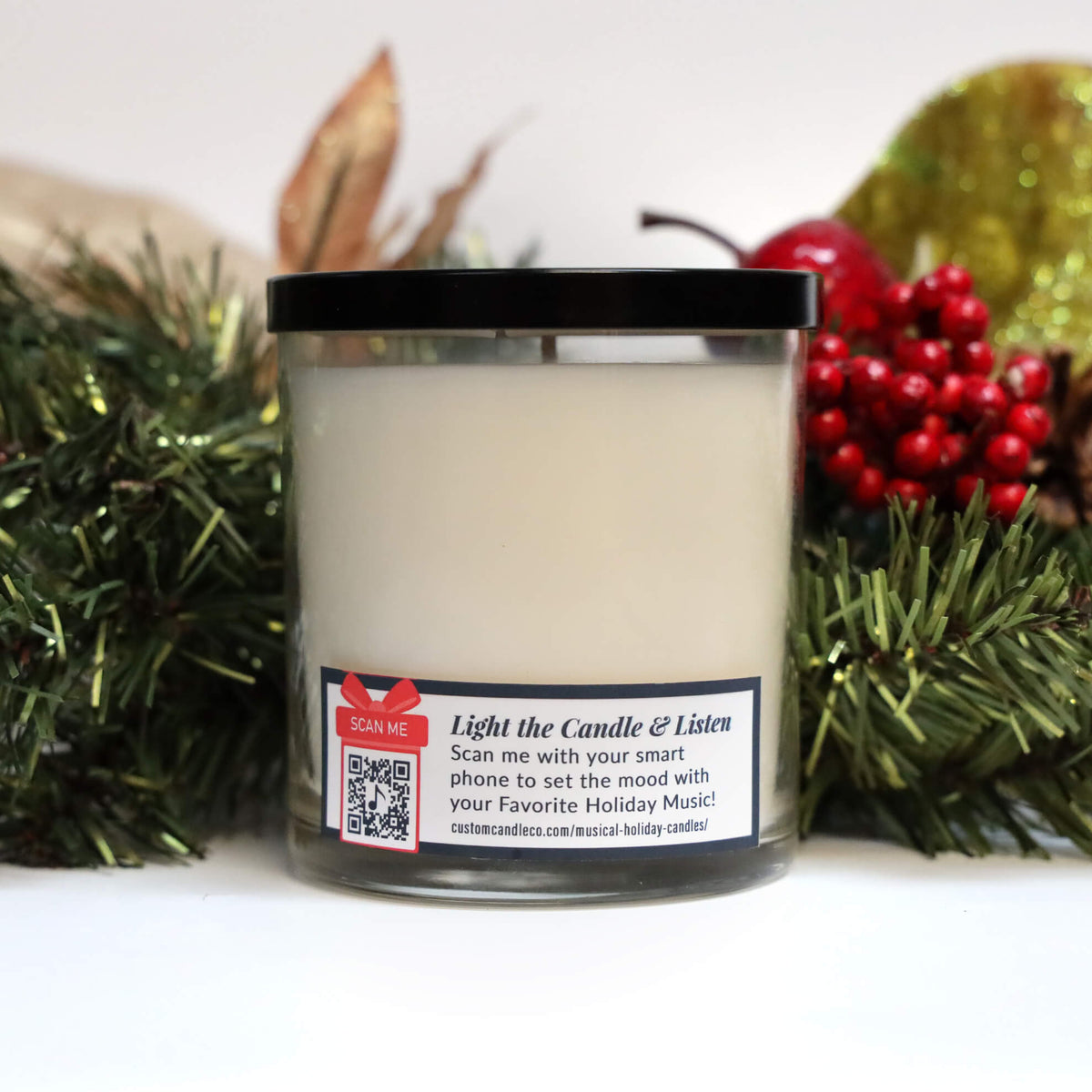 The Musical Holiday Candle & Diffuser | Jack Frost is a white candle in a glass jar with a QR code label, surrounded by festive greenery, red berries, and gold accents—ideal for bringing holiday charm to your space.