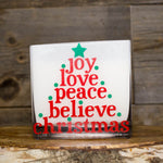 The "Frosted White Square – Love Joy Peace" candle comes in a glass holder with red and green text shaped like a Christmas tree, reading "joy love peace believe christmas," topped with a green star—ideal for festive cheer.