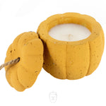 The Yellow Cement Pumpkin Candle features a white candle in a yellow pumpkin-shaped container with a removable lid beside it.