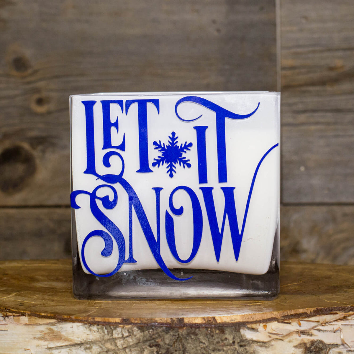The Frosted White Square – "Let It Snow" Candle features a white soy wax in a square glass holder with a blue snowflake and festive design—perfect as a holiday decoration or gift.