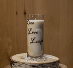 The Live Love Laugh Tall Candle sits on a wooden surface, surrounded by decorative clear gems and natural soy candles, creating a cozy atmosphere.