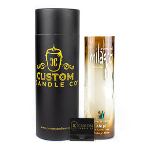 A black cylindrical box labeled "Custom Candle Co" stands next to a Recycled Desert-Colored Tequila Candle made from clear glass and a small black matchbox.