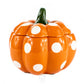 The Ceramic Mini Polka Orange Pumpkin Candle features an orange ceramic pumpkin with white polka dots and a green stem, displayed against a white background. This charming candle is perfect for adding autumn décor to any space.