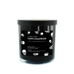 The Musical Halloween Candle – Candy Corn Black is a soy candle in a black jar with a black lid, featuring a label with white skulls and "Candy Corn Happy Halloween Custom Candle Co." text, set against a white background.