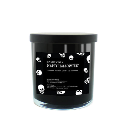 The Musical Halloween Candle – Candy Corn Black is a soy candle in a black jar with a black lid, featuring a label with white skulls and "Candy Corn Happy Halloween Custom Candle Co." text, set against a white background.