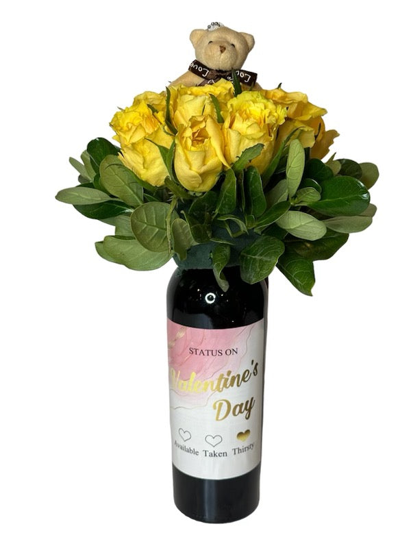 Wine and Flowers features a Cabernet bottle adorned with a label, topped with yellow roses, green leaves, and a cute teddy bear—an ideal romantic gift.