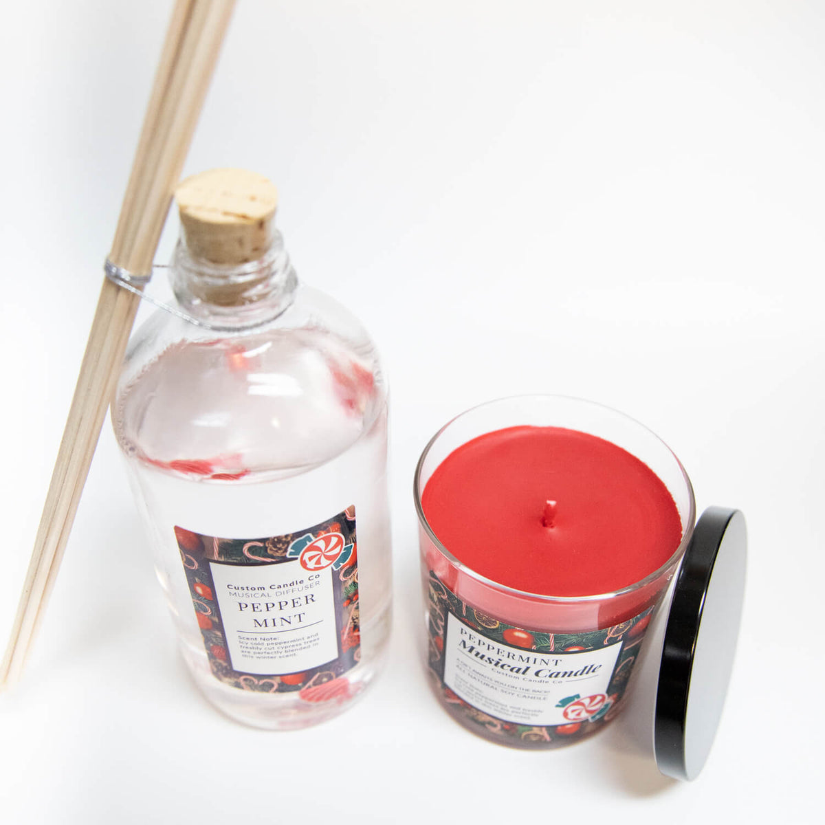 A Musical Holiday Candle & Diffuser | Peppermint set, featuring a clear diffuser with wooden sticks and a red candle in an open glass jar, is arranged on a white background.