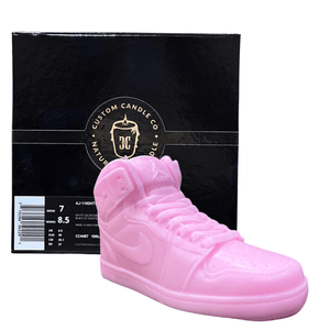 The AJ-1 Baby Pink Sneaker Candle – Large (On Backorder) is shown in front of a black box with Custom Candle Co.’s gold logo, offering a hand-poured candle that brings unique, stylish flair to any space.