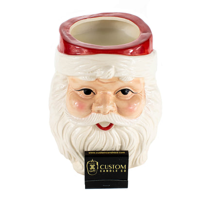 The Santa Claus Holiday Candle features an open-top ceramic Santa with a white beard and red hat, filled with all-natural soy wax and hand poured for the holidays, displayed with a Custom Candle Co. label.