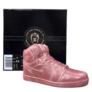 The AJ-1 Pink Shimmer Sneaker Candle (On Backorder), hand poured with all-natural wax, is displayed in front of a black Custom Candle Co. box featuring gold branding.