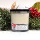 The Musical Holiday Candle & Diffuser | Sugar Cookie sits in a glass jar with a black lid before festive greenery and red berries. Its label includes a QR code with instructions to play holiday music.