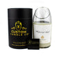 A hand-poured Recycled Champagne Candle in a glass jar sits beside a black cylindrical Custom Candle Co box with branding and contact info, plus a small black matchbox.
