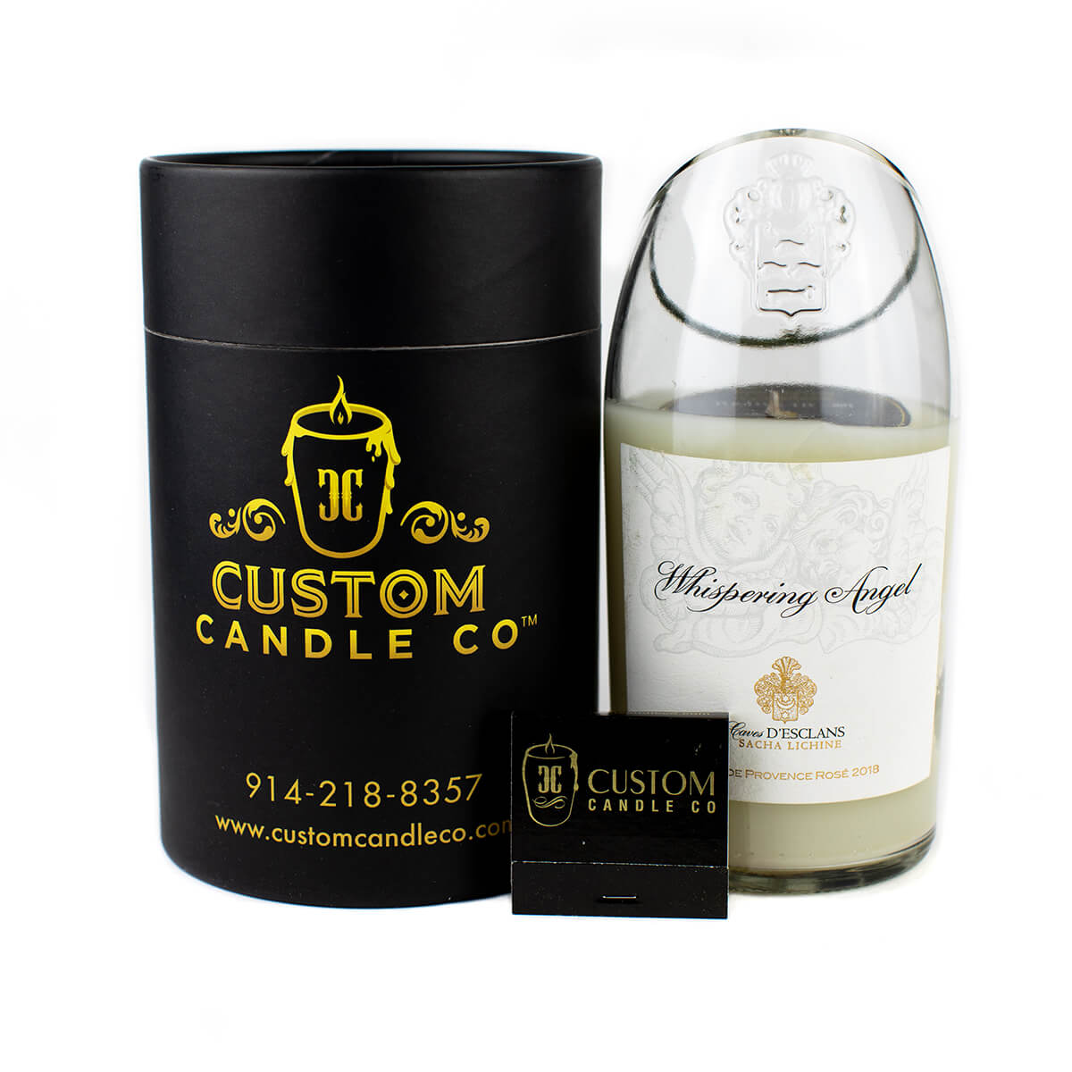 A hand-poured Recycled Champagne Candle in a glass jar sits beside a black cylindrical Custom Candle Co box with branding and contact info, plus a small black matchbox.