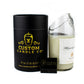 The Recycled Champagne Candle, a hand-poured white soy candle in a clear curved glass jar with a decorative label, is shown beside a black cylindrical box and matchbox, all featuring the Custom Candle Co. branding.
