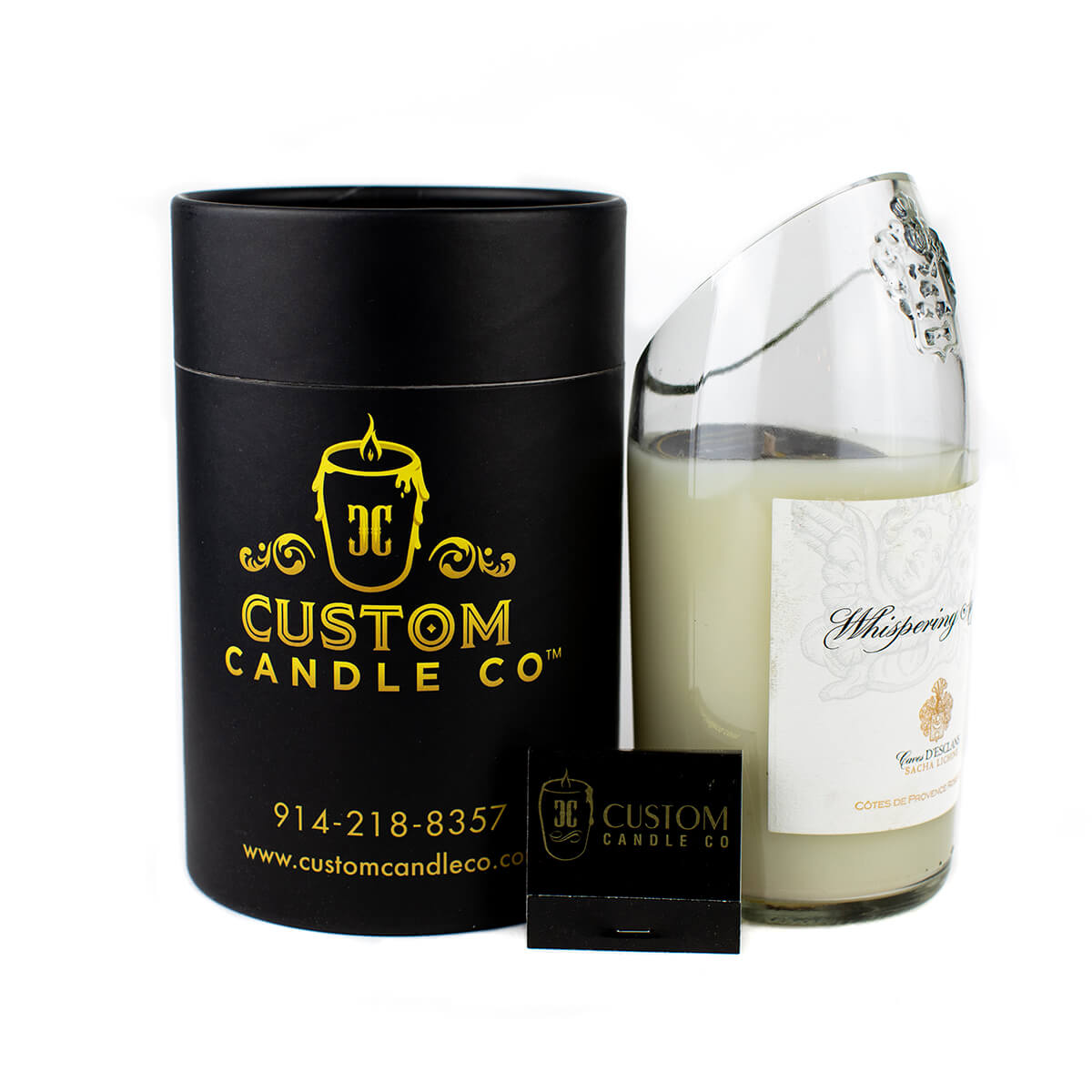 The Recycled Champagne Candle, a hand-poured white soy candle in a clear curved glass jar with a decorative label, is shown beside a black cylindrical box and matchbox, all featuring the Custom Candle Co. branding.