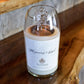 A hand poured Recycled Champagne Candle with a white label sits on a wooden surface. The label displays the product name and design details in light gray text.