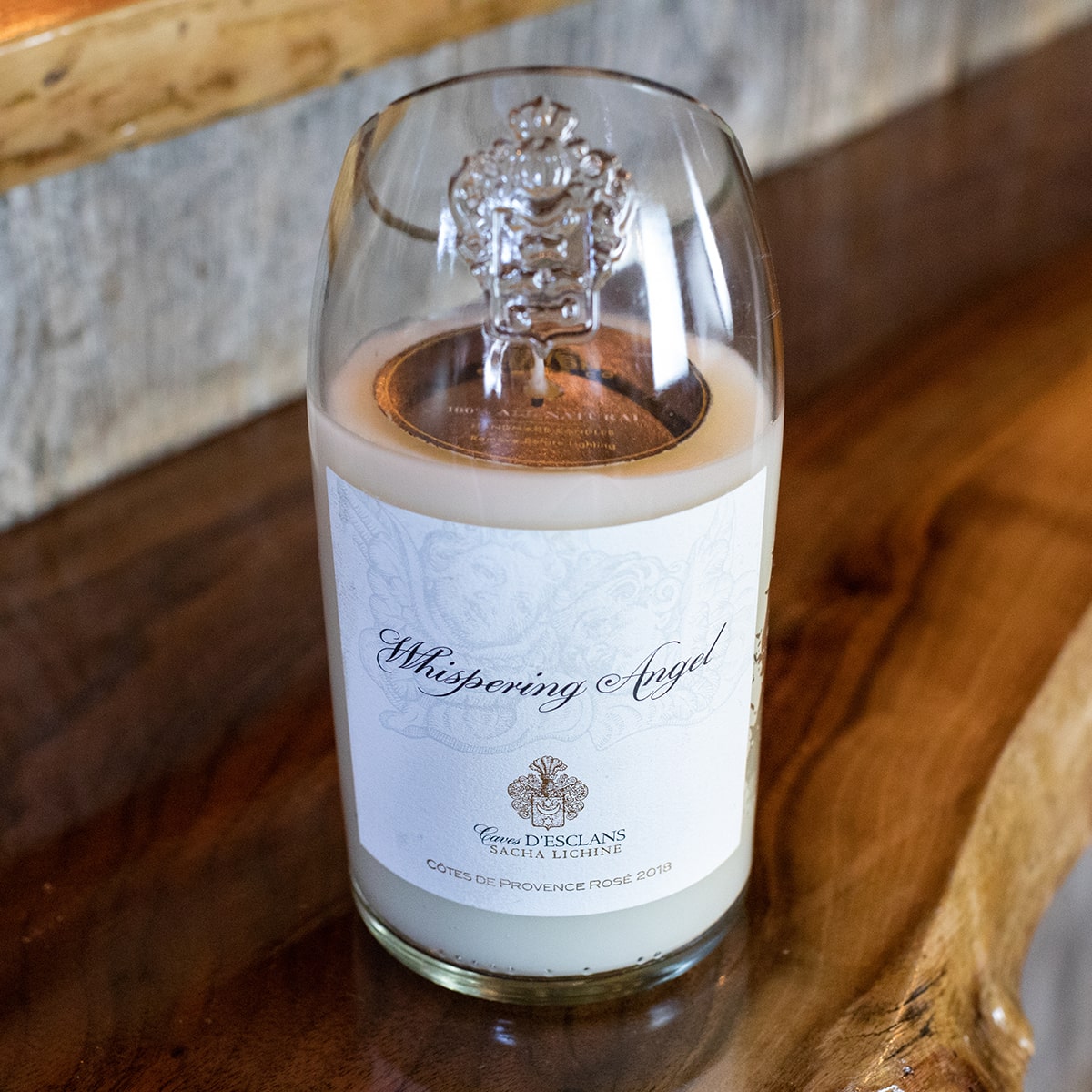 A hand poured Recycled Champagne Candle with a white label sits on a wooden surface. The label displays the product name and design details in light gray text.