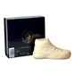 The AJ-11 White Hightop Sneaker Candle – Large (On Backorder), hand poured in a cream hue, is shown before a black box with gold and white branding. This candle features the signature Black Ice fragrance.