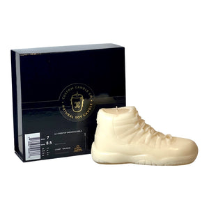 The AJ-11 White Hightop Sneaker Candle – Large (On Backorder), hand poured in a cream hue, is shown before a black box with gold and white branding. This candle features the signature Black Ice fragrance.