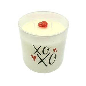 The XOXO Colored Quote Candle is a hand-poured soy wax candle in a frosted tumbler jar, featuring "xoxo" and red hearts design, two wicks, and a small red heart on top—making it a sweet gift.