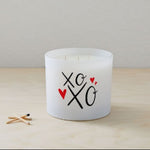 The XOXO Colored Quote Candle comes in a frosted tumbler jar with "xo xo" and two red hearts on the glass, hand-poured for charm and warmth—perfect for any space.